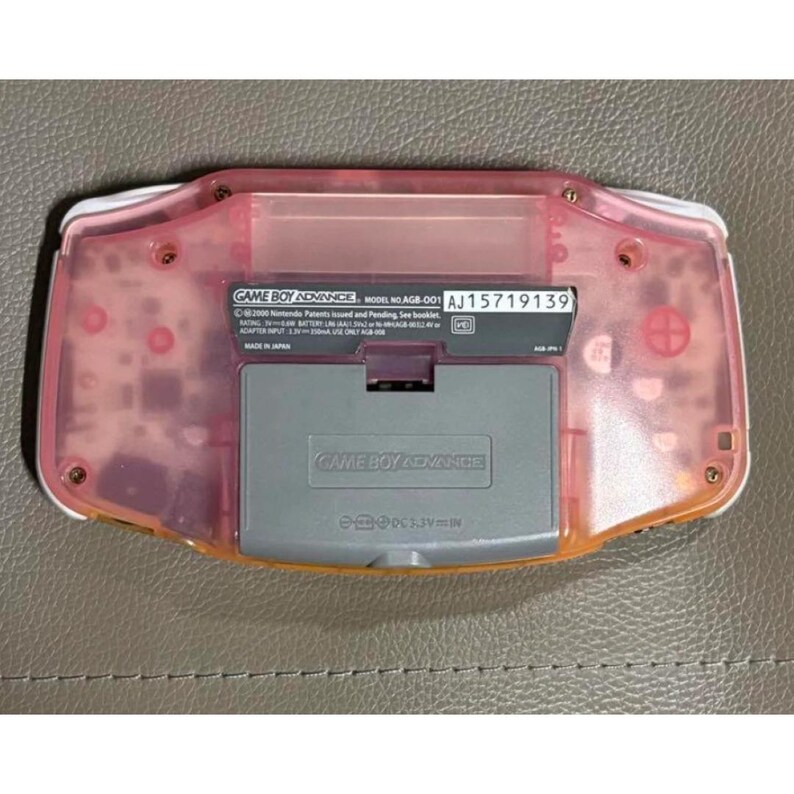 May include: A pink Game Boy Advance console, viewed from the back. The battery compartment and internal components are visible through the translucent pink casing. Model number AGB-001, serial number AJ15719139.