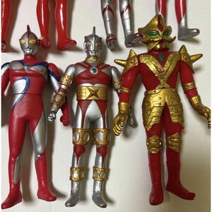 May include: Three standing action figures featuring humanoid designs. The left figure is red and silver with blue accents. The center figure is silver and red with gold circular details. The right figure is red with gold armor plating and green eyes.