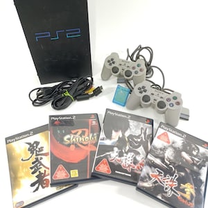 May include: A black PlayStation 2 console with the PS2 logo, two gray controllers, game discs, and cables. The game cases feature Japanese text and colorful graphics. A memory card is also included.