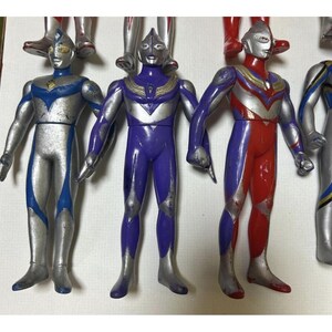 May include: A collection of three standing Ultraman action figures. The left figure is silver and blue, the center figure is purple and silver, and the right figure is red, purple, and silver. Each figure features a distinct mask and chest emblem.