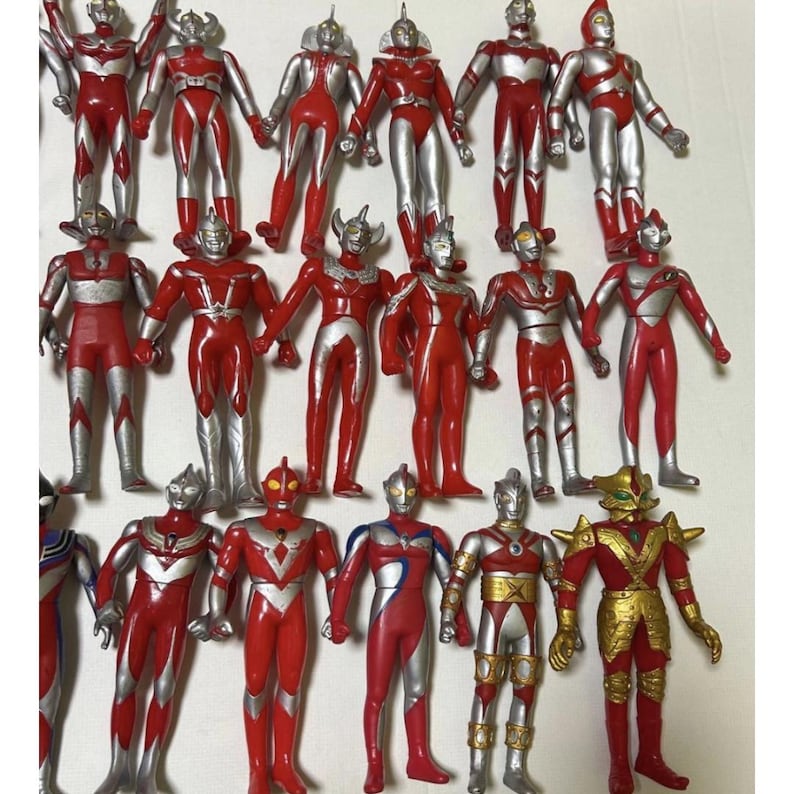 May include: A collection of seventeen Ultraman action figures arranged in three rows. Each figure features a red and silver color scheme with distinct head designs, chest emblems, and limb patterns. One figure on the bottom right wears gold armor.