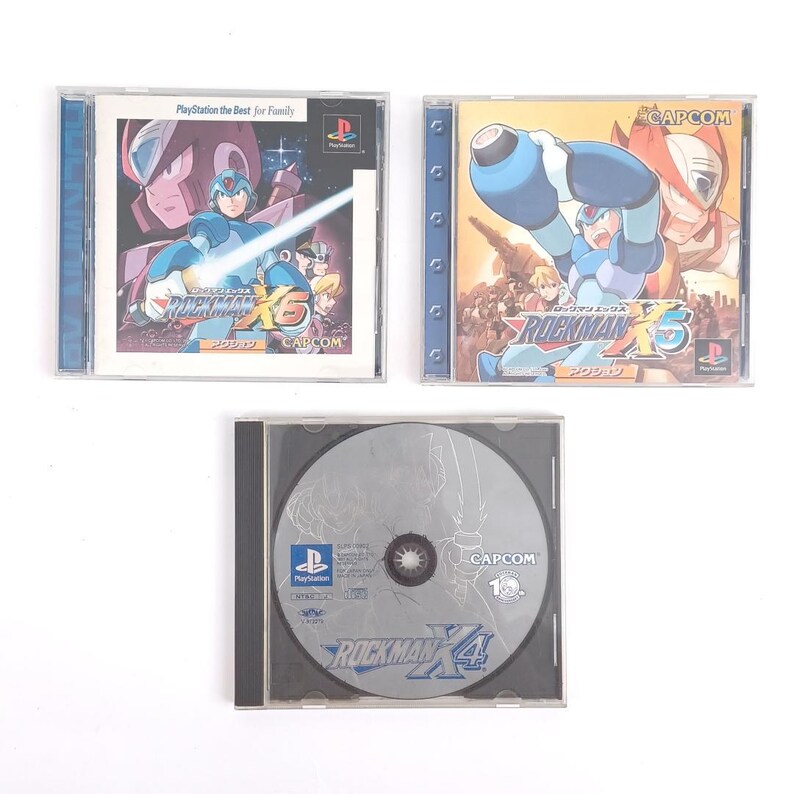 Puede incluir: Tres cajas de juegos de video para la consola PlayStation. Las cajas son azules, amarillas y negras. La parte frontal de las cajas presenta al personaje de videojuego Mega Man. El texto en las cajas dice "Rockman X6" y "Rockman X4".