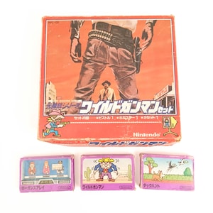 May include: A vintage Nintendo Wild Gunman game set. The box features a cowboy illustration. Three game cartridges are below, each with colourful illustrations and Japanese text. The set includes a pistol, holster, and cassette.