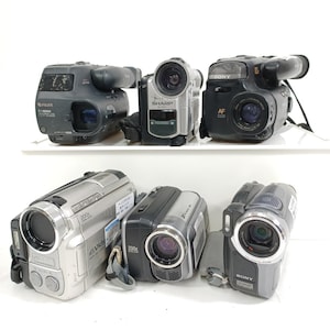 Könnte beinhalten: Eine Sammlung von sechs Vintage-Camcordern in verschiedenen Farben, darunter Silber, Schwarz und Grau. Die Camcorder haben Objektive, Sucher und verschiedene Knöpfe und Regler. Zu den Marken gehören Sony, Sharp und Fuji.