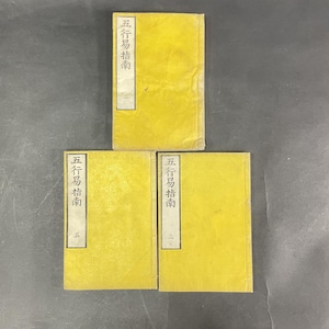 May include: Three rectangular books with yellow covers, each featuring a white vertical label on the left side containing black Chinese characters. The books are arranged in a triangular formation, with one positioned above two others, displaying consistent text.