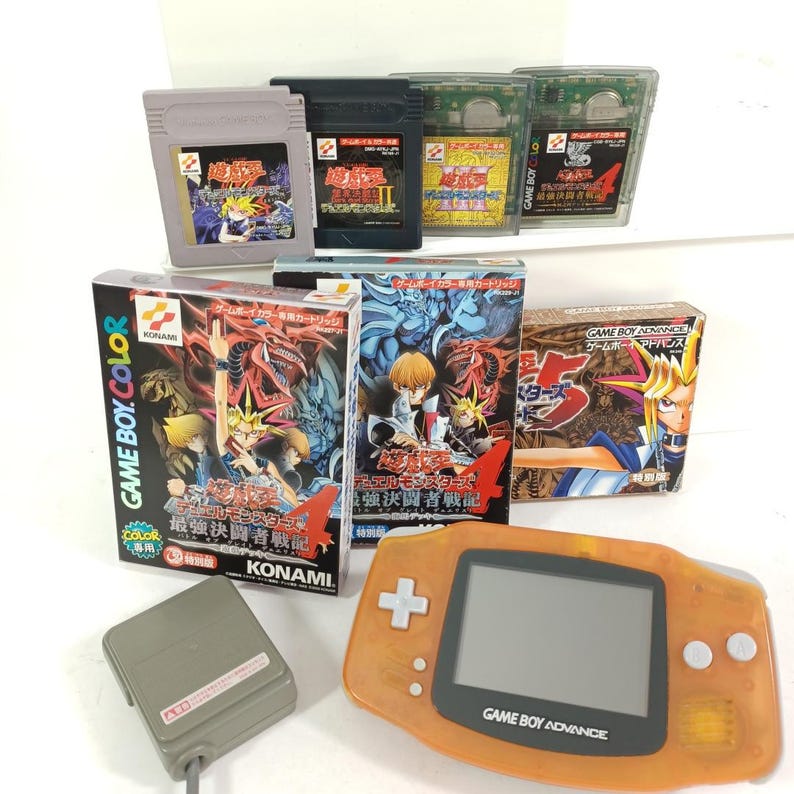 May include: A selection of retro Game Boy and Game Boy Advance items. Includes various game cartridges, boxes, and an orange Game Boy Advance console. The boxes feature colourful illustrations and Japanese text. A grey controller is also present.