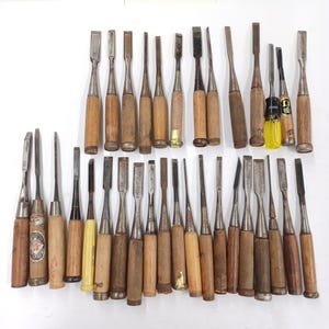 May include: A collection of thirty-two wood chisels with metal blades and wooden handles, including one chisel with a yellow plastic handle. The tools vary in blade width and handle length, featuring metallic ferrules and some Japanese text labels.