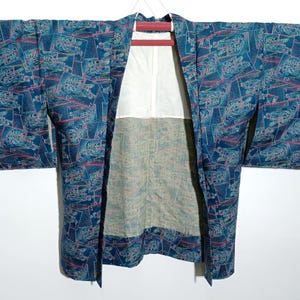 Puede incluir: Kimono vintage en tonos azules, turquesas y rosas, con un patrón repetitivo de paisaje. El kimono está abierto, revelando un forro blanco y un interior estampado. Colgado en una percha roja.