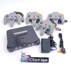 Puede incluir: Un conjunto completo de consola de juegos Nintendo 64, que incluye una consola gris, cuatro mandos grises con botones coloridos, un adaptador de corriente y cables. El conjunto incluye el texto "(E) Earst Japan".