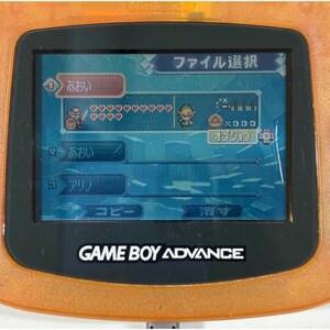 May include: An orange Game Boy Advance console showing a game menu with Japanese text. The screen displays character icons, health bars, and menu options. The console's logo, "GAME BOY ADVANCE," is visible.