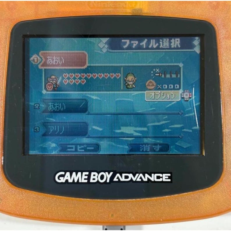 May include: An orange Game Boy Advance console showing a game menu with Japanese text. The screen displays character icons, health bars, and menu options. The console's logo, "GAME BOY ADVANCE," is visible.