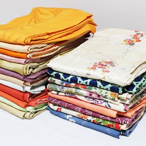 Op de afbeelding: Een stapel kleurrijke stof, waarschijnlijk voor het maken van kimono's, met verschillende patronen en texturen. De stof is netjes gevouwen en in een stapel gerangschikt.