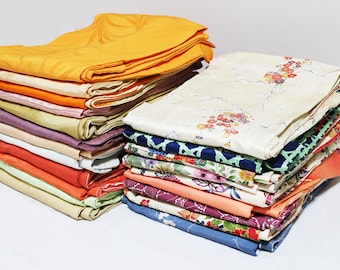 Puede incluir: Una pila de tela colorida, probablemente para hacer kimonos, con una variedad de patrones y texturas. La tela está doblada cuidadosamente y dispuesta en una pila.