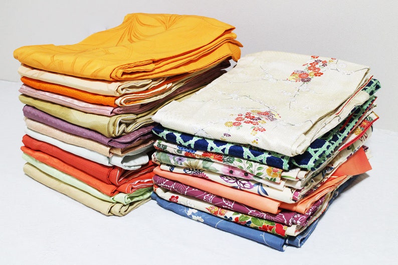 Op de afbeelding: Een stapel kleurrijke stof, waarschijnlijk voor het maken van kimono's, met verschillende patronen en texturen. De stof is netjes gevouwen en in een stapel gerangschikt.