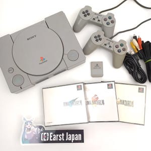 Könnte beinhalten: Eine graue PlayStation 1 Konsole mit zwei passenden Controllern, einer Speicherkarte und drei Spielhüllen. Die Spielhüllen sind mit "Final Fantasy VII" und "Final Fantasy IX" beschriftet. Kabel und ein Aufkleber mit japanischem Text sind ebenfalls vorhanden.