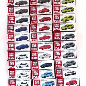 Puede incluir: Colección de coches modelo en miniatura en sus cajas originales. Las cajas rojas y blancas, con texto japonés, presentan varios modelos de coches en diferentes colores, incluyendo gris, rojo, azul y amarillo.
