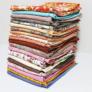 Op de afbeelding: Een stapel kleurrijke stoffenresten, waarschijnlijk van vintage kimono's, met verschillende patronen en texturen. De stoffen zijn netjes gevouwen en in een stapel gelegd.