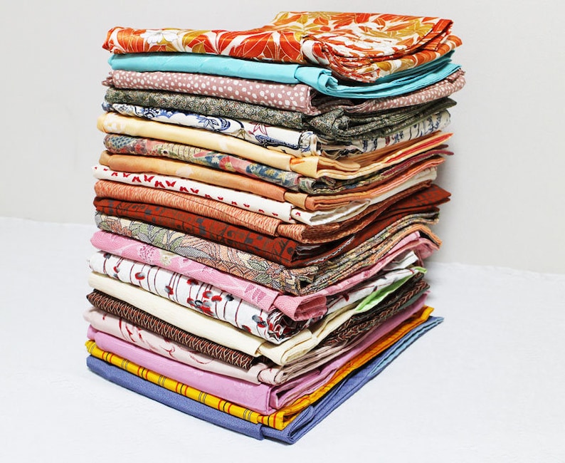 Op de afbeelding: Een stapel kleurrijke stoffenresten, waarschijnlijk van vintage kimono's, met verschillende patronen en texturen. De stoffen zijn netjes gevouwen en in een stapel gelegd.