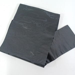 Può includere: Un tessuto nero piegato con un sottile motivo a onde. Il tessuto è di un colore scuro e uniforme con una lucentezza, e il motivo a onde è leggermente più scuro del colore di base. Il tessuto è probabilmente utilizzato per abbigliamento o arredamento.