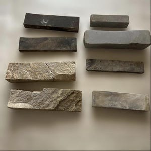 Peut inclure: Une collection de pierres à aiguiser rectangulaires de différentes tailles et textures, dans des tons de gris, de brun et de noir. Certaines pierres présentent des signes d'usure et ont une forme incurvée.