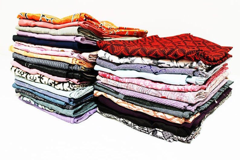 May include: Two stacks of folded fabric items in various colors and patterns. The stacks include items in shades of orange, pink, black, purple, and white. The fabrics have different textures and designs, including geometric and floral prints.