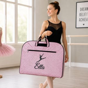 Teenage dancer holding a personalized pink glitter garment bag with custom name and dance silhouette, custom dance competition travel bag for costumes and recital wear.