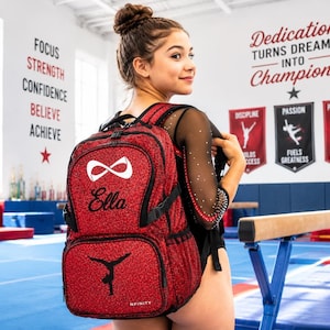 May include: A red glitter backpack featuring a white infinity symbol, the name Ella in black script, and a black silhouette of a gymnast performing a handstand. The bag includes black zippers, adjustable straps, and the brand name Nfinity.