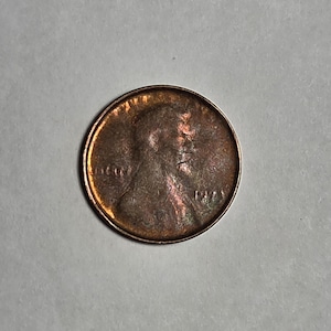 May include: A copper-colored United States one-cent coin featuring the profile of Abraham Lincoln facing right. The coin displays the word LIBERTY on the left side, the phrase IN GOD WE TRUST at the top, and the year 1944 on the right side.