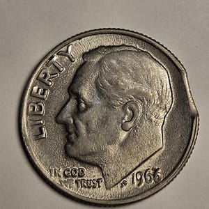 May include: A silver-colored 1966 United States dime coin featuring the profile of Franklin D. Roosevelt facing left. The word LIBERTY is embossed on the left side, with IN GOD WE TRUST and the year 1966 visible. The coin has a noticeable clipped edge.