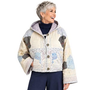 May include: A quilted hooded jacket featuring a patchwork design with cream, blue, and grey fabric panels. The jacket has long sleeves, a front button closure with four round buttons, and two front pockets. The interior lining is a light grey fabric.