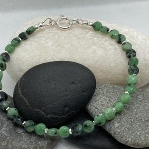May include: A green and black gemstone bracelet with silver accents. The bracelet is made of round beads and has a silver clasp.
