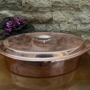 May include: A copper oval baking dish with a lid. The dish has a shiny, polished finish and a silver knob on the lid.