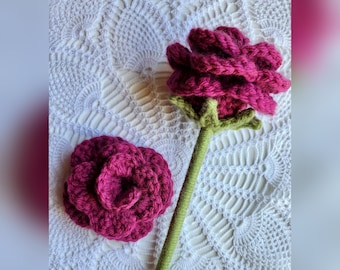 May include: Two crocheted roses, one with a stem, on a white crocheted surface. The roses are a deep pink color.