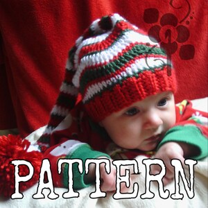 Può includere: Un bambino che indossa un cappello da elfo a uncinetto a righe rosse, bianche e verdi con una lunga punta a punta e un pon pon in cima. Il bambino indossa anche un maglione natalizio rosso e verde. L'immagine ha la parola "PATTERN" scritta in lettere bianche su uno sfondo bianco.
