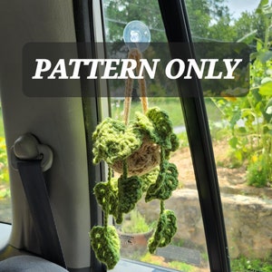 May include: A crocheted hanging plant with green leaves and a brown pot. The plant is hanging from a suction cup on a car window. The text "PATTERN ONLY" is displayed on the image.