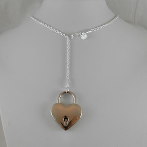 May include: A silver heart-shaped padlock necklace with a silver chain. The padlock has a keyhole and is attached to a silver chain that is adjustable in length.