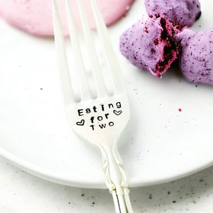 May include: A silver fork with the words "Eating for two" engraved on the handle. The fork is on a white plate with a pink and purple dessert.