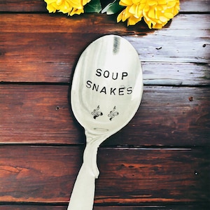 May include: A silver soup spoon with the words "Soup Snakes" engraved on the bowl. Two small snake illustrations are also engraved on the spoon.