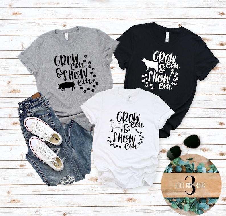 Peut inclure: Trois t-shirts avec des silhouettes d'animaux diff&eacute;rentes et le texte "Grow 'em & Show 'em" imprim&eacute; en noir. Les t-shirts sont gris, noir et blanc.