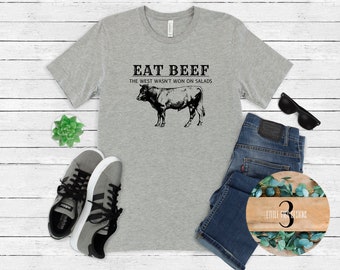 May include: A gray t-shirt with the text "Eat Beef The West Wasn't Won On Salads" and a black and white illustration of a cow.