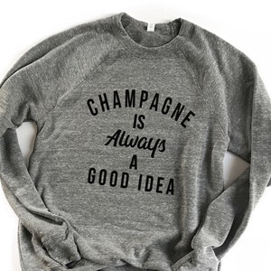 May include: Gray sweatshirt with the text "Champagne is always a good idea" printed in black.