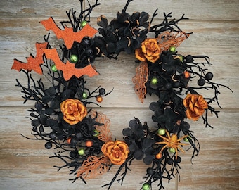 May include: A black twig wreath decorated with orange fabric flowers, green berries, and black bats.