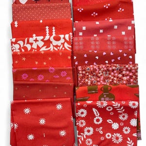 Op de afbeelding: Een verzameling rode stoffen vierkanten met verschillende patronen, waaronder aardbeien, stippen, bloemmotieven en zonnen. De stoffen zijn gevouwen en gestapeld, met een verscheidenheid aan texturen en prints. Ideaal voor quilt- en knutselprojecten.