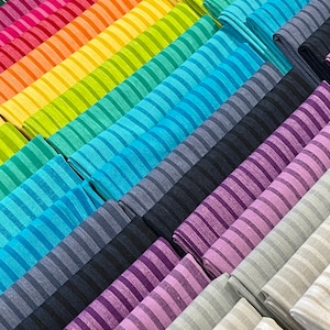 Könnte beinhalten: Eine Regenbogen-Auswahl an gestreiften Stoffproben, gefaltet und in einem Farbverlauf gestapelt. Die Farben reichen von Rot über Rosa, Orange, Gelb, Grün, Blau, Lila bis Grau.