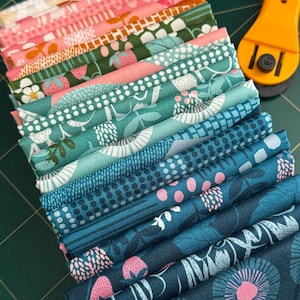 Puede incluir: Una pila de cuadrados de tela doblados con varios patrones florales y botánicos. La paleta de colores incluye rosa, verde y turquesa. Un cortador rotatorio amarillo sugiere costura o acolchado.