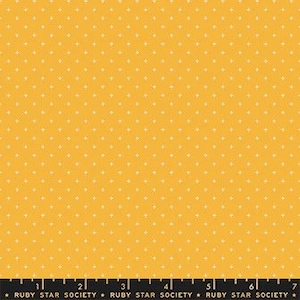 May include: A close-up of yellow fabric with a repeating pattern of small, white triangles. The fabric has a smooth texture and is evenly lit. A black ruler with white markings is at the bottom.
