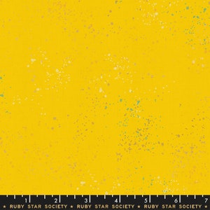 May include: Bright yellow fabric with a speckled pattern. The fabric has a textured appearance, with small, irregular spots of white, gold, and teal scattered across the surface. The text "RUBY STAR SOCIETY" is printed at the bottom.