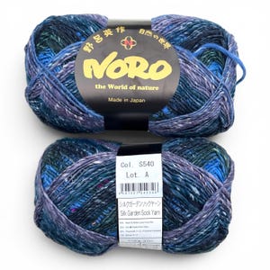 May include: Two skeins of Noro Silk Garden Sock Yarn in a variegated blend of deep blue, teal, purple, and green. The black paper labels feature the text Noro the World of nature, Made in Japan, Col. S540, Lot. A, and Silk Garden Sock Yarn.