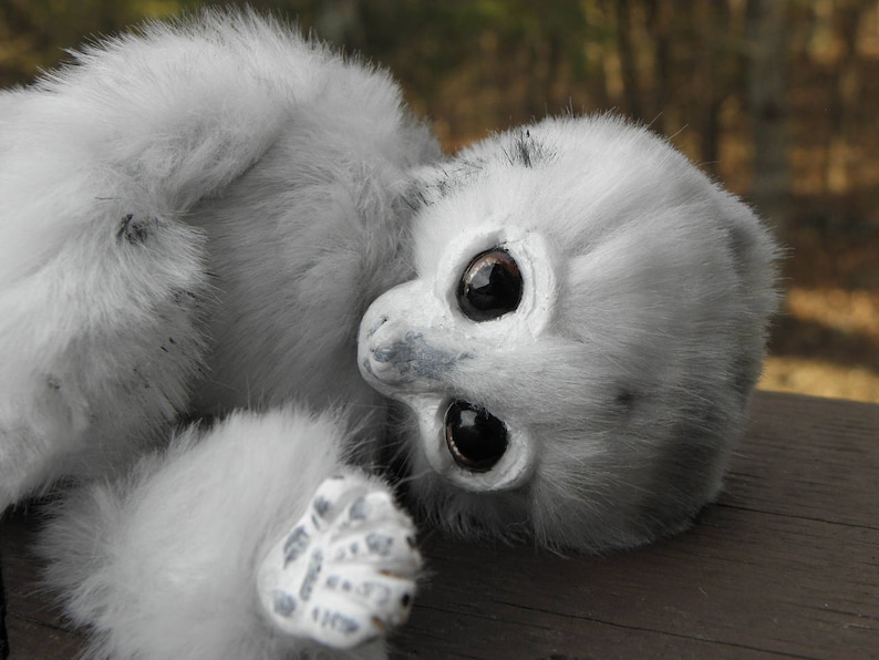 May include: A white, fluffy stuffed animal with large black eyes and a grey nose. The animal is lying on its side with its head turned to the side.