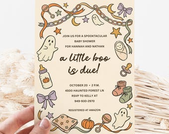 May include: A cream-colored baby shower invitation card featuring illustrations of ghosts, pumpkins, baby bottles, rattles, bows, and stars. The text reads: JOIN US FOR A SPOOKTACULAR BABY SHOWER FOR HANNAH AND NATHAN, a little boo is due!, OCTOBER 20, 2 P.M., 4500 HAUNTED FOREST LN, RSVP TO KELLY AT 949-930-2970, REGISTERED AT AMAZON.